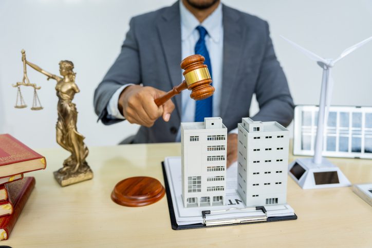 A male Asian lawyer in a formal suit works at his desk, focusing on contracts, legal matters, and urban planning issues such as building models, zoning, ordinances, and municipal regulations.