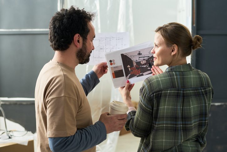 Rear view of young woman with interior sketches looking at her husband during discussion of home renovation ideas